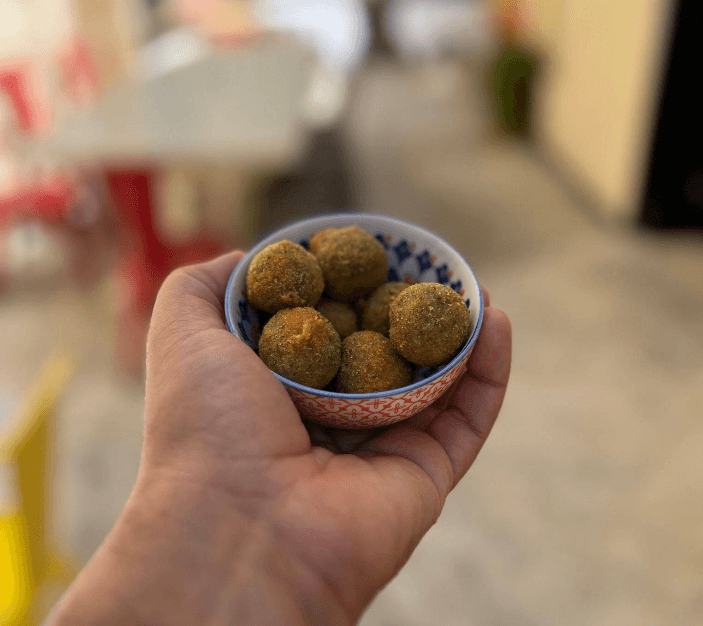 Una mano tiene una ciotolina di ceramica con olive ascolane fritte e dorate all'aperto.